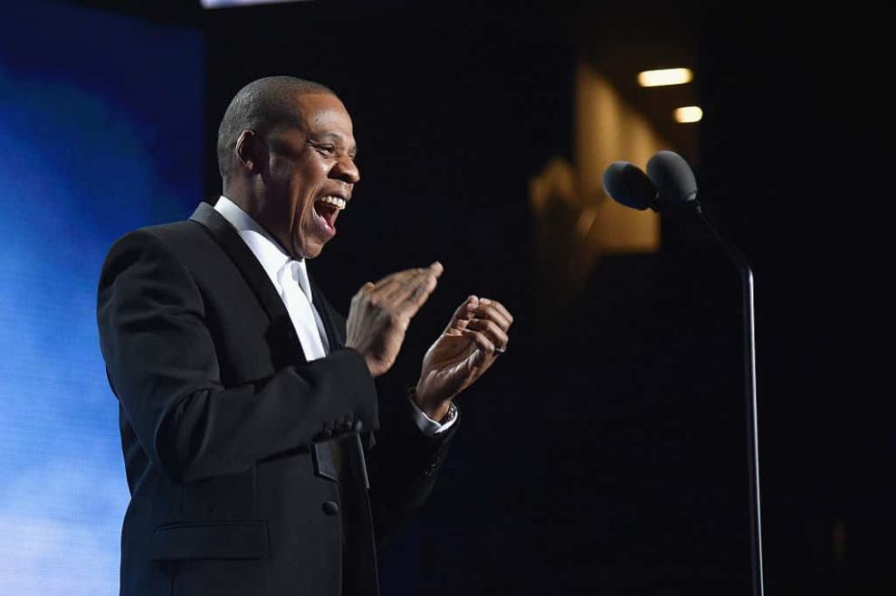 Jay Z in tux clapping on stage in front of microphone