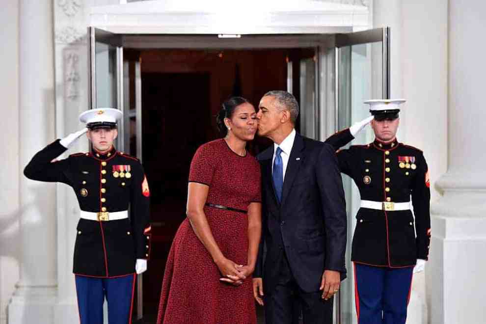 Barack Obama kissing Michelle Obama on the cheek in front of two marines standing guard