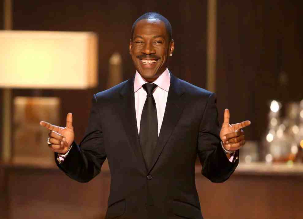Eddie Murphy in suit pointing with both hands in front of a bar
