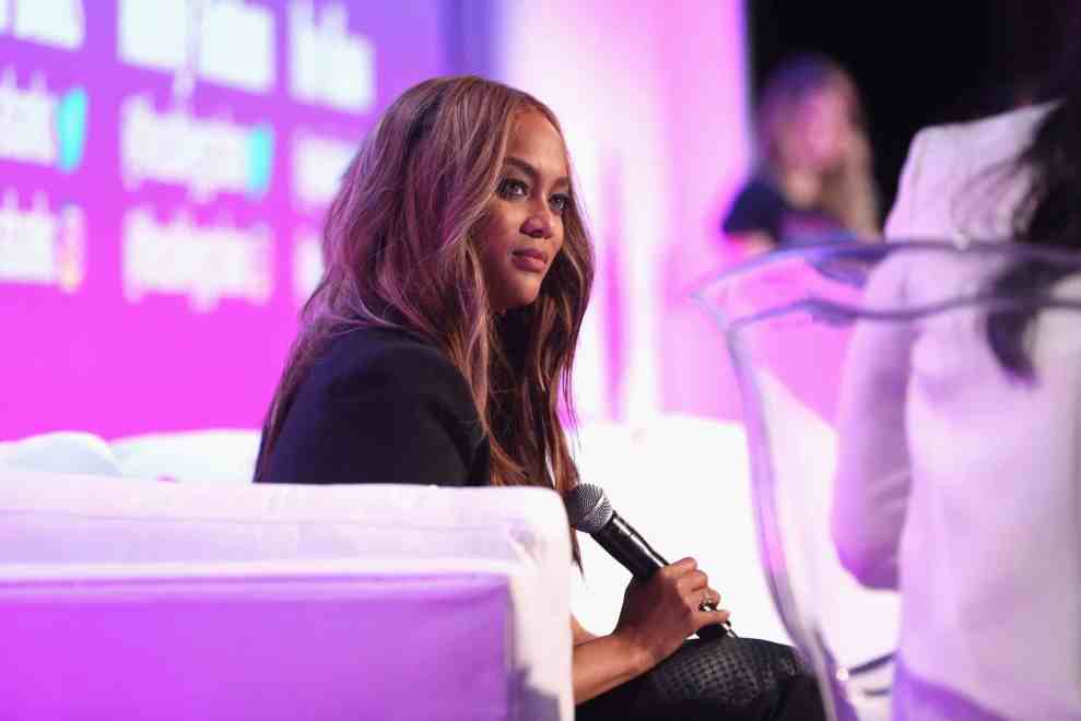 Tyra Banks in white chair in front of purple background