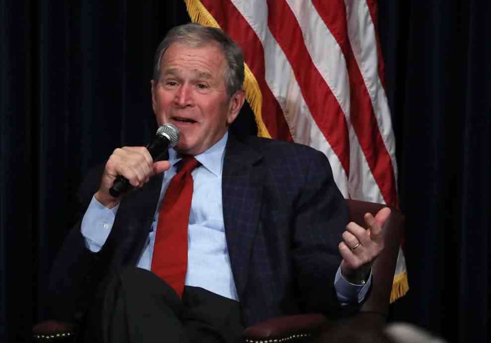 George W. Bush speaking into microphone while sitting in front of American flag