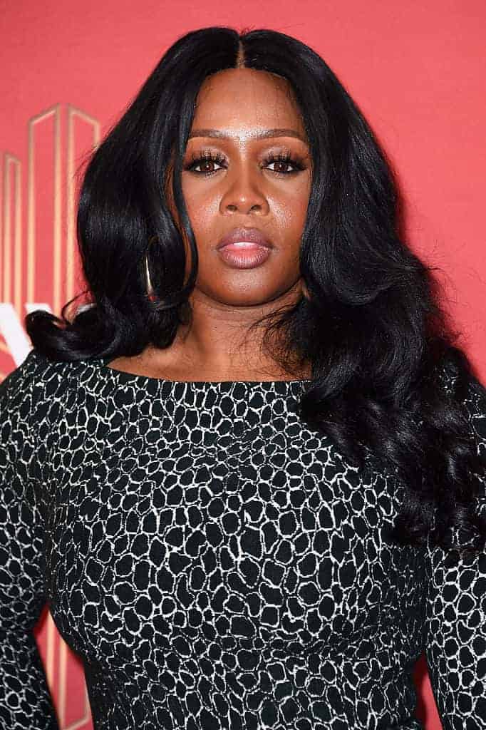 Remy Ma in black dress in front of red background