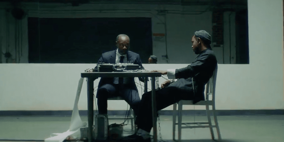 Screen shot from DAMN video showing Kendrick Lamar sitting at table taking lie detector test with Don Cheadle administering test