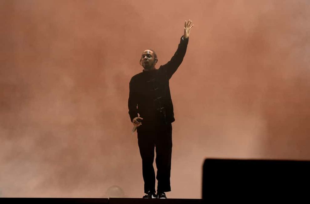 Kendrick Lamar on stage in all black with smoky orange background
