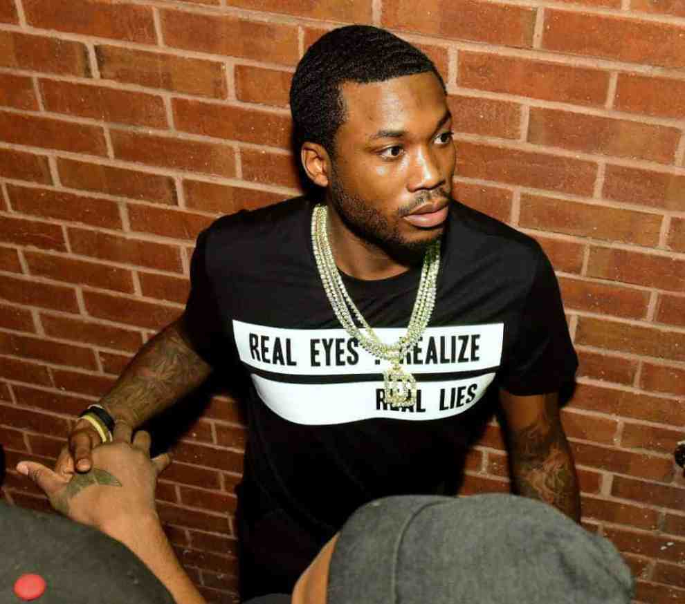 Meek Mill in front of brick background wearing t-shirt reading "Real Eye - Realize - Real Lies