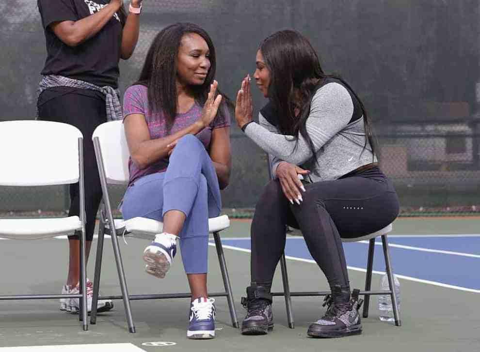 Venus Williams giving high five to Serena Williams while sitting in casual clothes