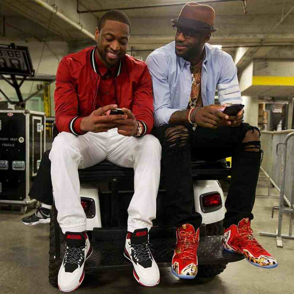 Dwayne Wade and LeBron James on their cell phones sitting together on  a car