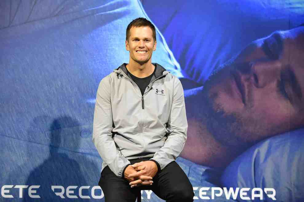Tom Brady in front of sreenshot from his Under Armor commercial for recovery sleepwear