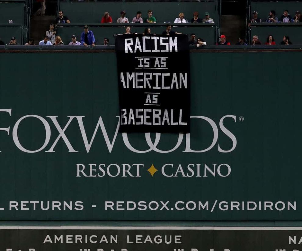 Sign hanging over the green wall at Fenway Park in Boston reading "Racism Is As American as Baseball"