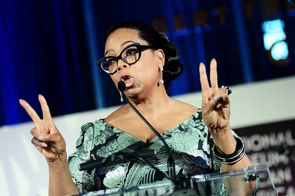 Oprah speaking at podium and giving two peace signs
