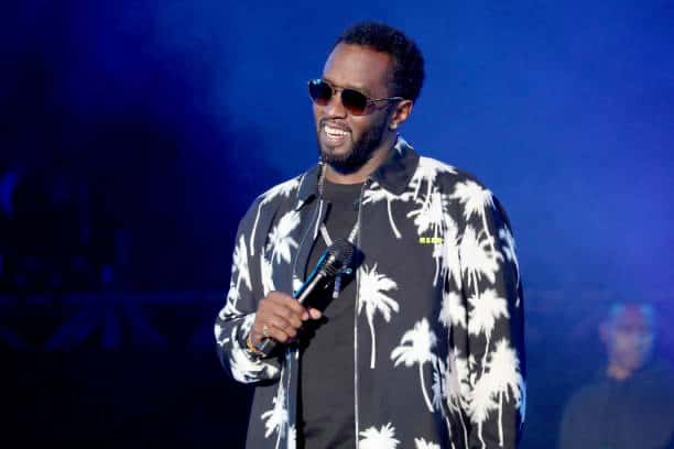 Diddy on stage wearing black and white and smiling with a microphone