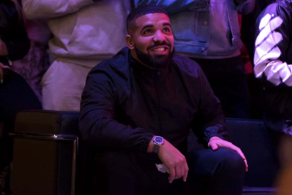 Drake sitting down wearing a black suit