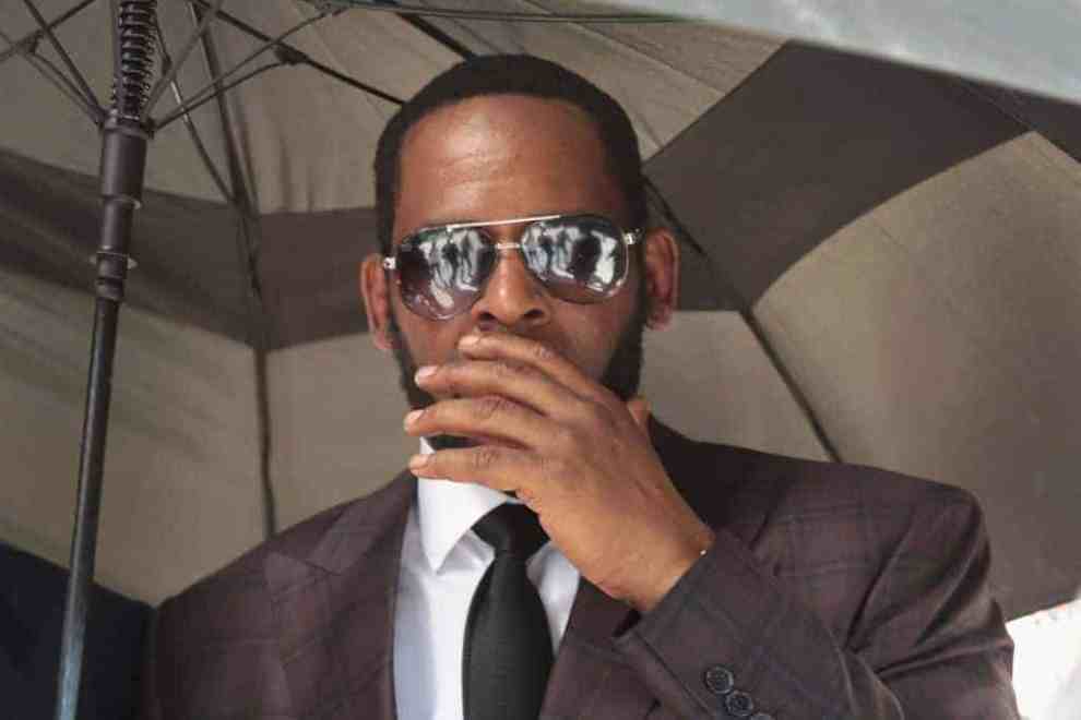 R&B singer R. Kelly covers his mouth as he speaks to members of his entourage as he leaves the Leighton Criminal Courts Building following a hearing on June 26