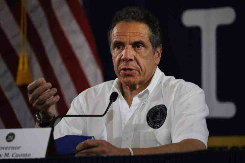 Governor Cuomo wearing white shirt sitting at a microphone