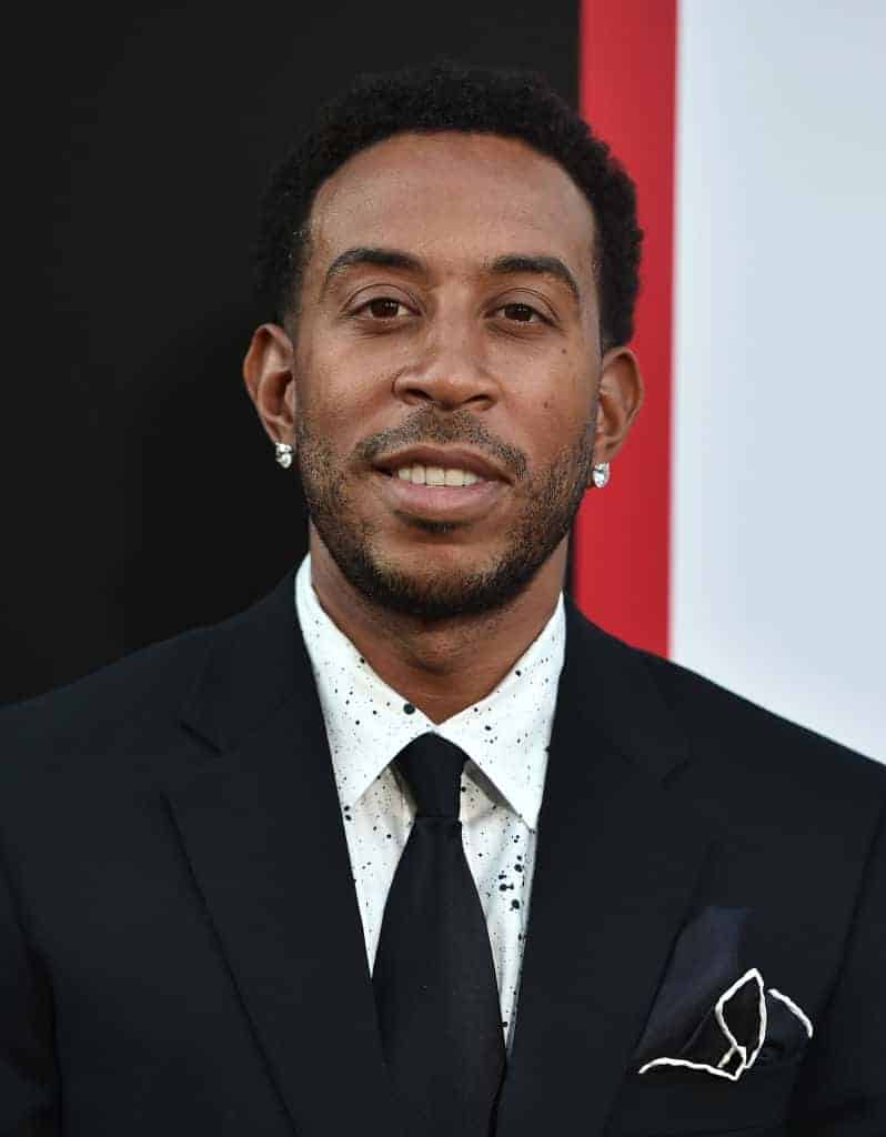 Ludacris smiling wearing a black suit with a black tie and white shirt