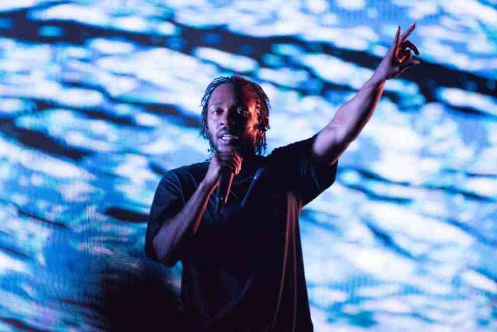 Kendrick Lamar on stage wearing a black shirt in front of blue screen