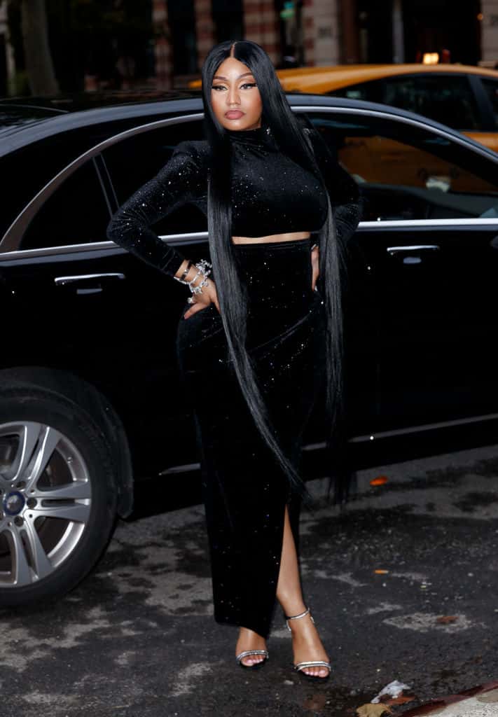 Nicki Minaj wear an all black standing in front of a car.