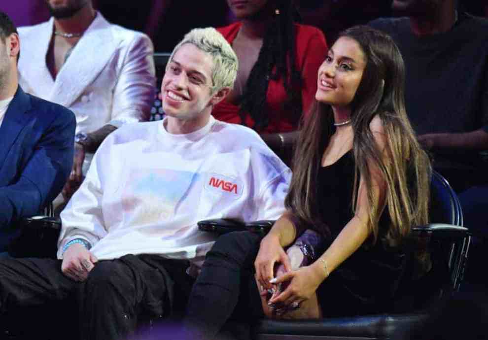 Ariana Grande and Pete Davidson holding hands while seated in an audience