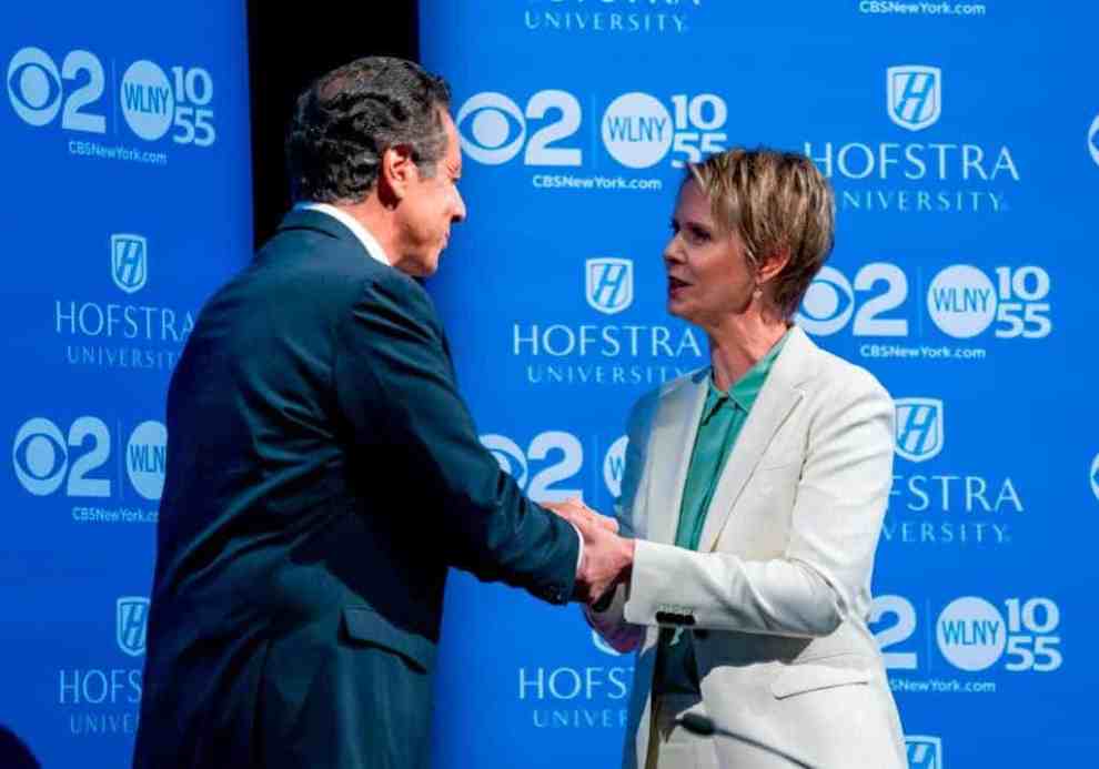 Andrew Cuomo and Cynthia Nixon shaking hands on stage in front of a blue background