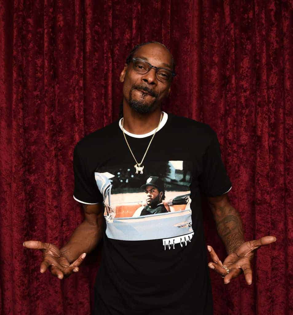 Snoop Dogg wearing a black shirt standing in front of a red curtain