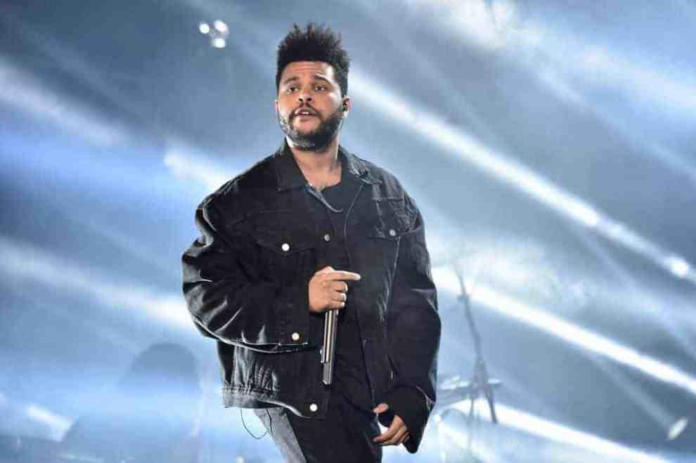 The Weeknd wearing all black performing on stage.