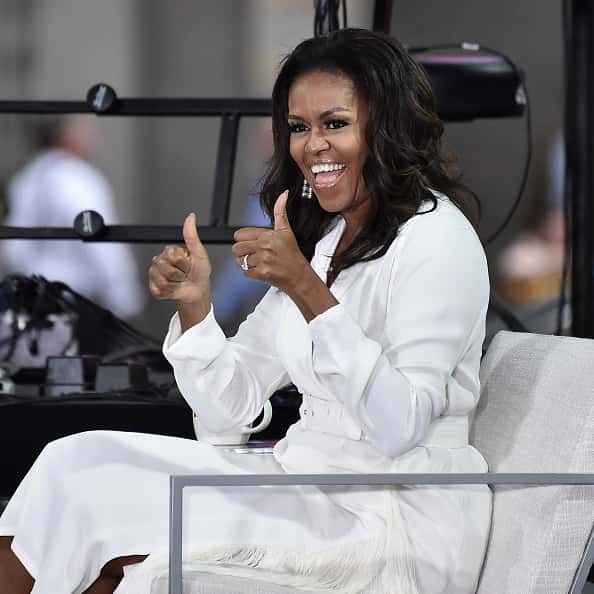 Michelle Obama in all white sitting in chair giving two thumbs up