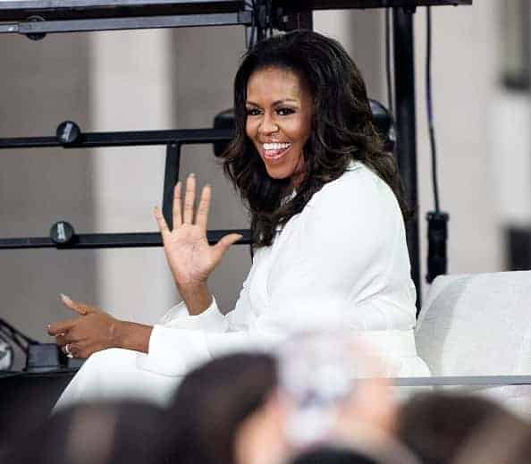 Michelle Obama in all white sitting in chair waving