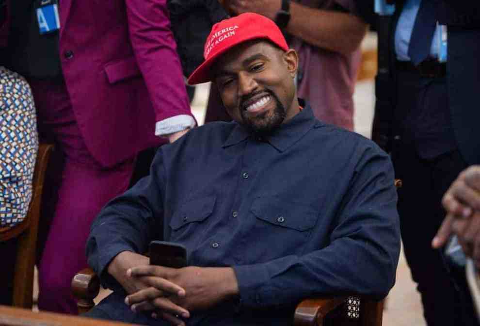 Kanye West wearing blue shirt and a MAGA hat