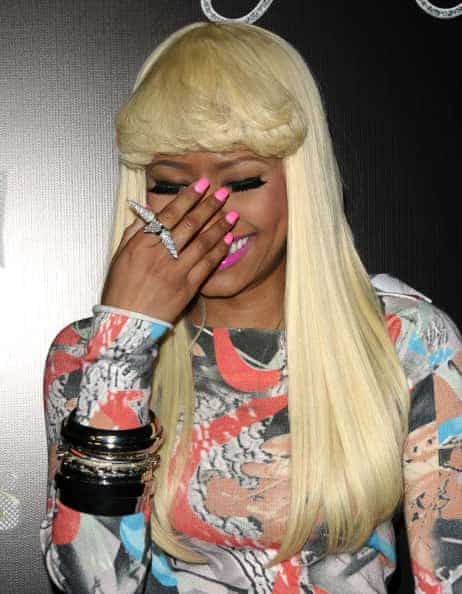 Nicki Minaj covering face with hand wearing blond wig and multicolored dress