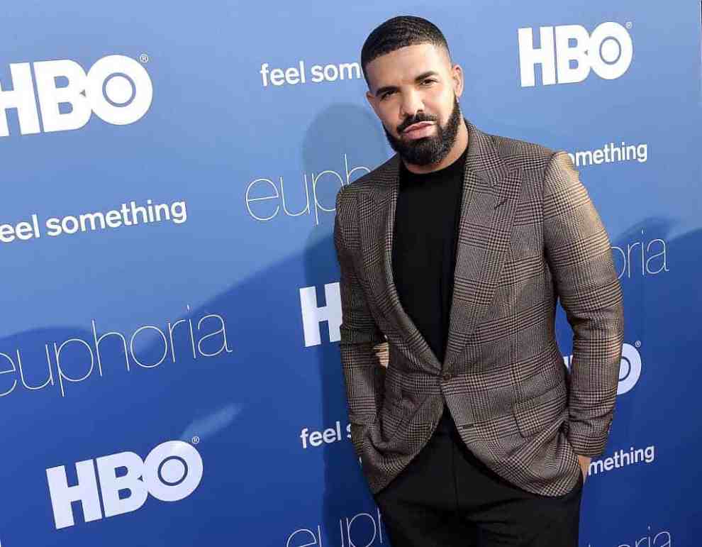 Drake wearing black and brown standing front of a blue and white backdrop