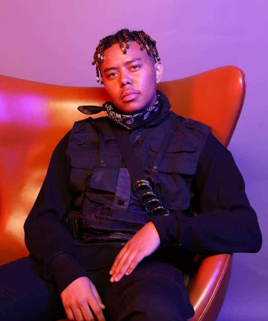 YBN Cordae sitting in a red chair wearing all black