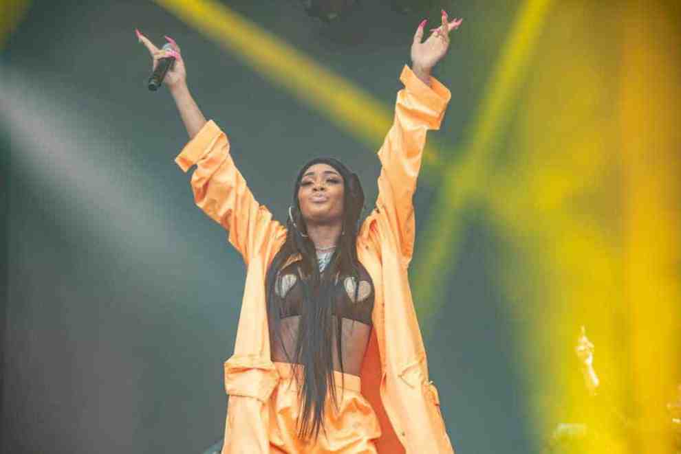 Saweetie standing on stage wearing orange