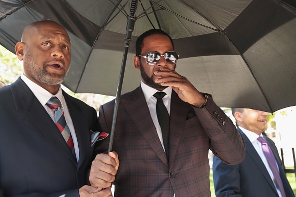 R&B singer R. Kelly covers his mouth as he speaks to members of his entourage as he leaves the Leighton Criminal Courts Building following a hearing on June 26
