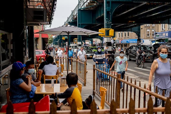 Pedestrians wearing protective masks pass in front of customers sitting outside to eat at a restaurant in the Corona neighborhood in the Queens borough of New York