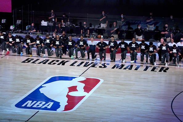 Members of the Milwaukee Bucks and the Boston Celtics kneel around a Black Lives Matter logo before the start of an NBA basketball game Friday