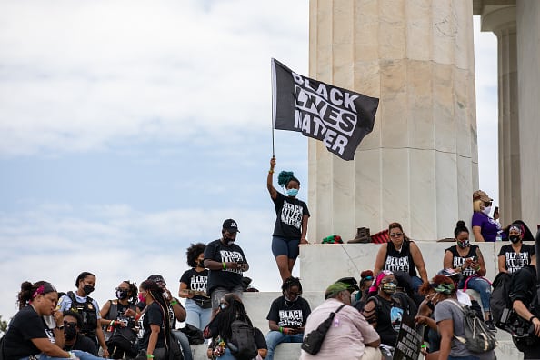 A demonstrator wearing a protective mask waves a "Black Lives Matter" flag on the steps of the Lincoln Memorial during the "Get Your Knee Off Our Necks" March on Washington in Washington