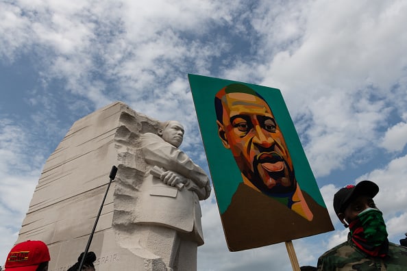 A demonstrator wearing a protective mask holds a painting of George Floyd at Martin Luther King Jr. memorial during the "Get Your Knee Off Our Necks" March on Washington in Washington