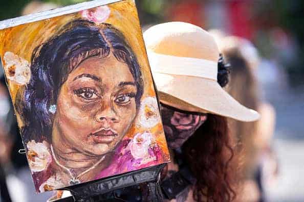 Artist Claudine Anrather wearing a mask holds her hand painted sign tribute to Breonna Taylor in Union Square Park