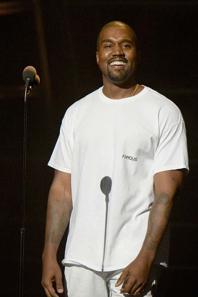 Kanye West Wearing All white standing in front of a microphone.