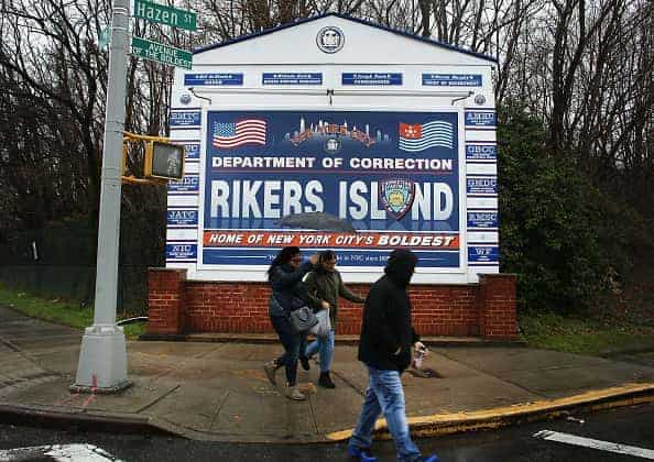 People walk by a sign at the entrance to Rikers Island on March 31