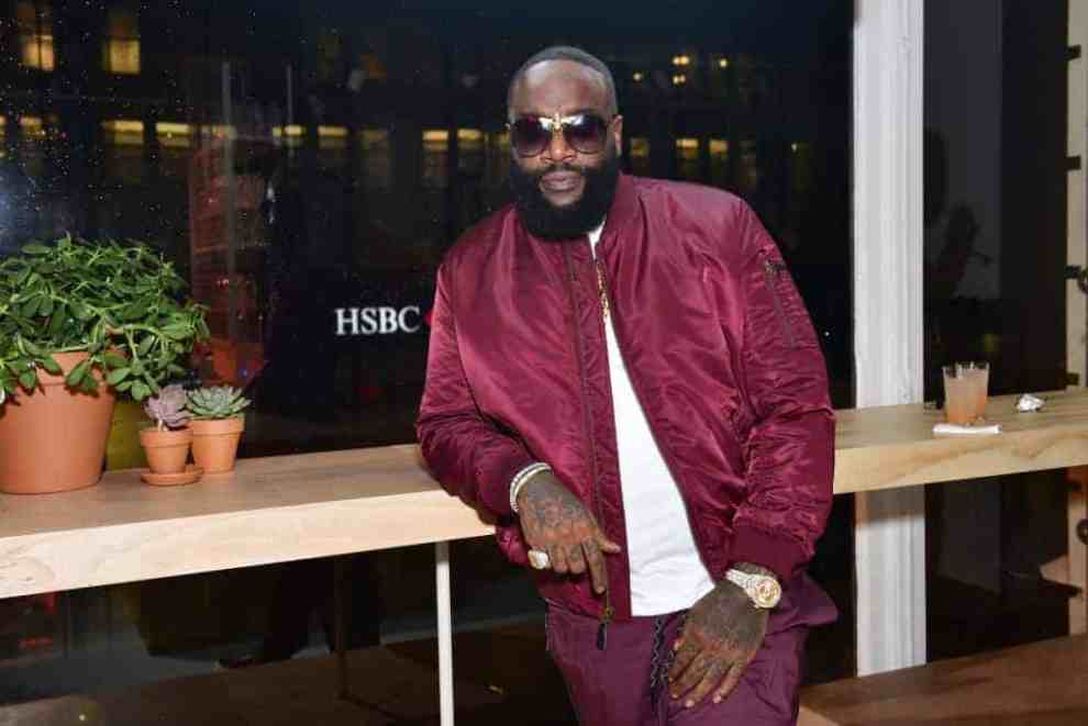 Rick Ross poses in maroon jacket and white t-shirt