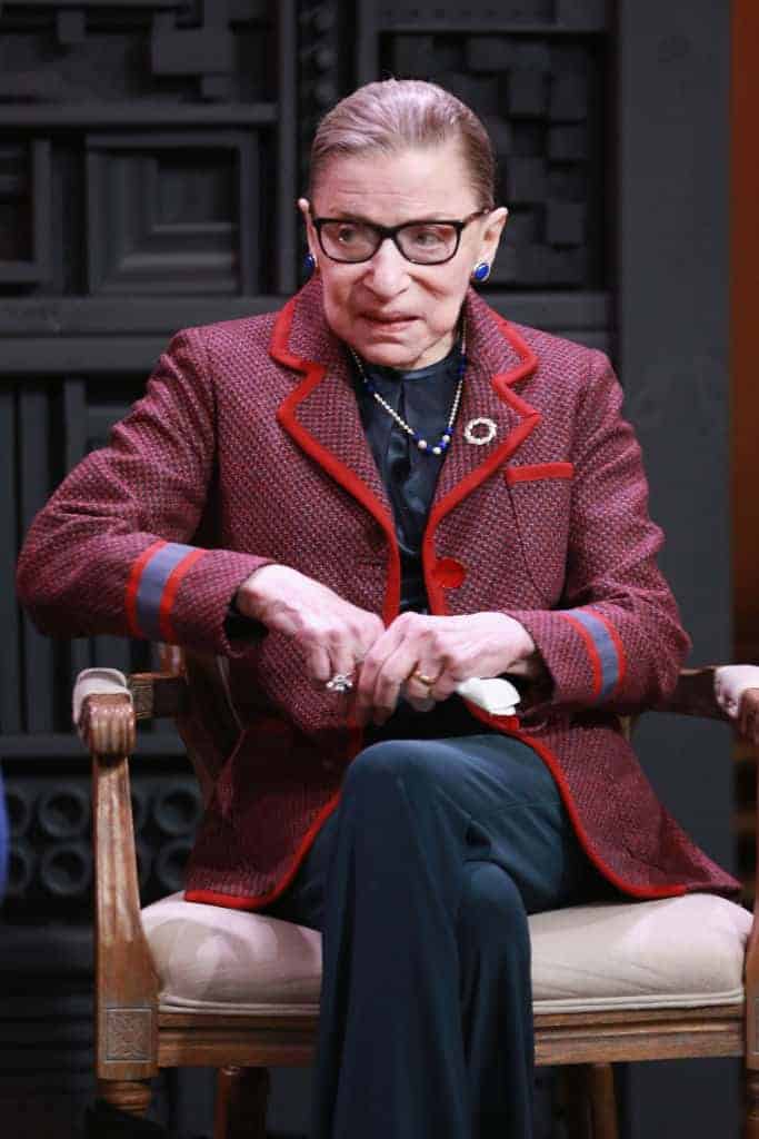 Ruth Bader Ginsberg wearing a red Jacket sitting in a chair