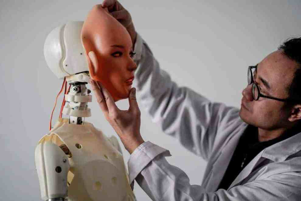 Lab worker putting rubber face over plastic skeleton with Wires to start forming full sex doll