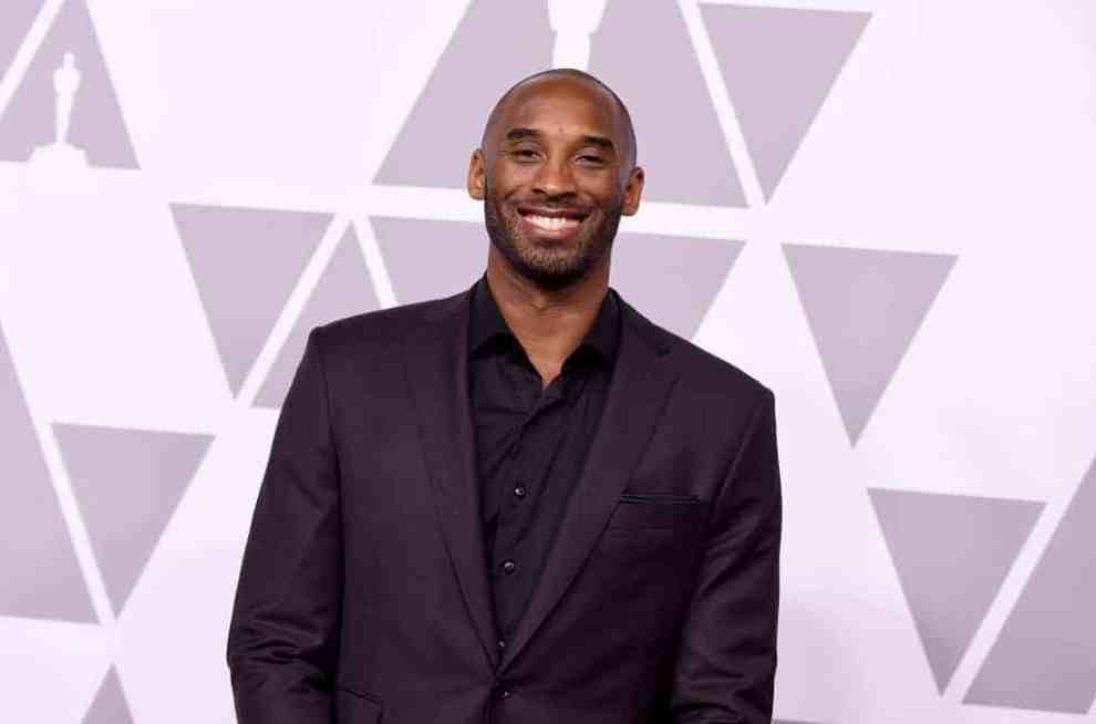 Kobe Bryant smiling at the camera wearing a burgundy suit