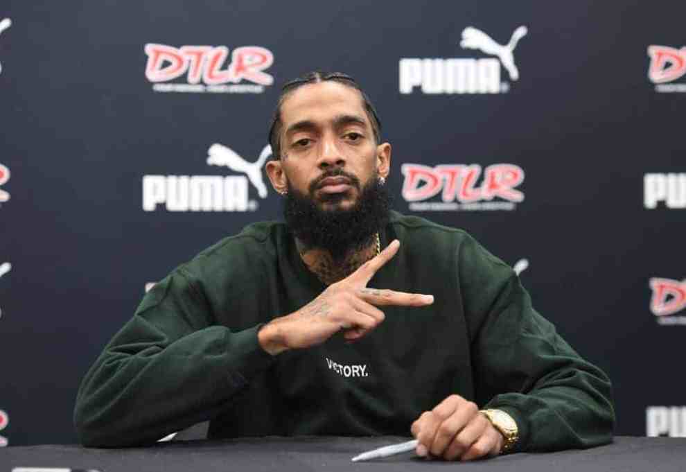 Nipsey Hussle showing the peace sign while wearing a green sweatshirt