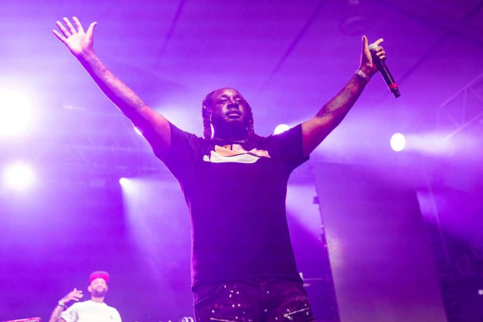 T-Pain standing on stage with his arms stretched out in front of a purple light