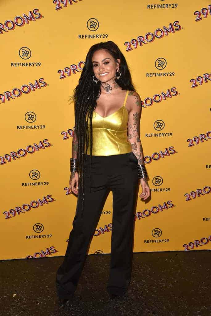 Kehlani wearing a yellow shirt and black pants standing in front of yellow and black background