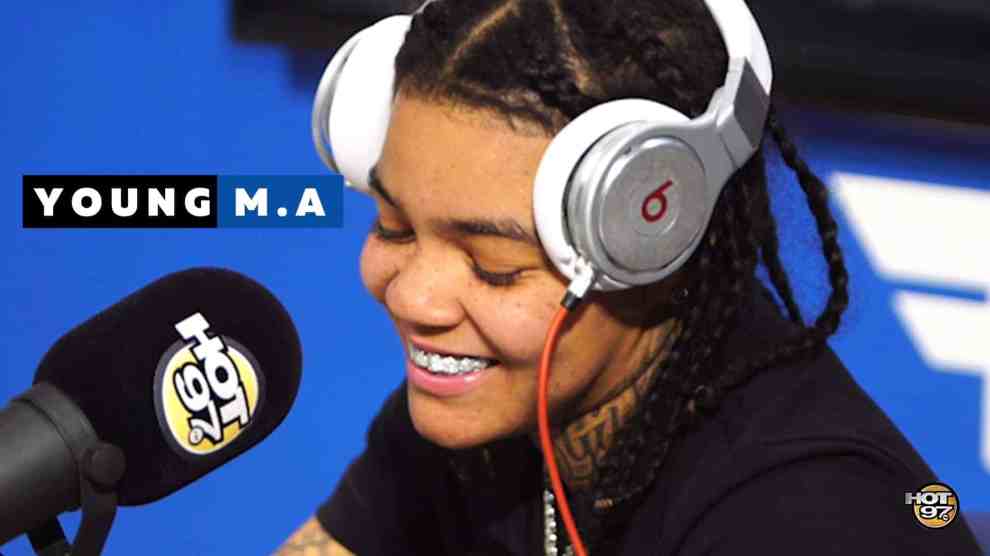 American rapper Young MA smiling with a diamond grill piece in front of a microphone